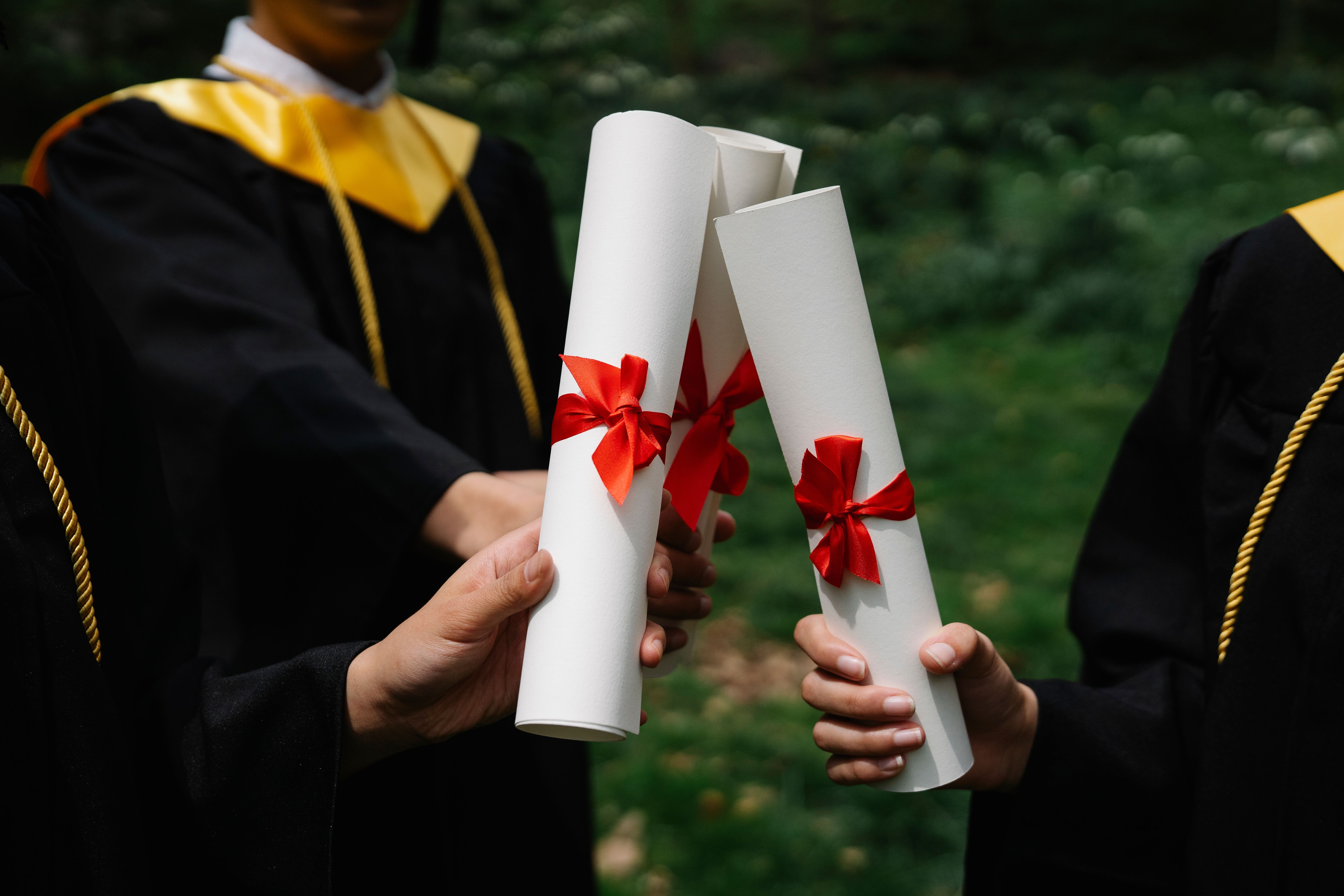 Group of MBA graduates holding diplomas during an outdoor graduation ceremony